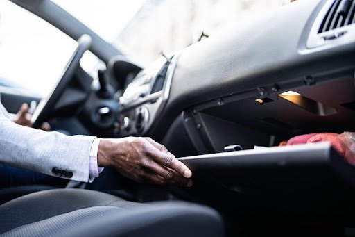 Main d'un conducteur ouvrant la boîte à gants de sa voiture sur le tableau de bord.