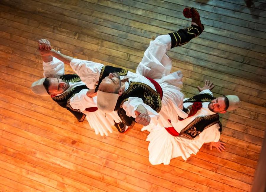 Danseurs albanais en costume traditionnel exécutant une danse folklorique sur une scène en bois