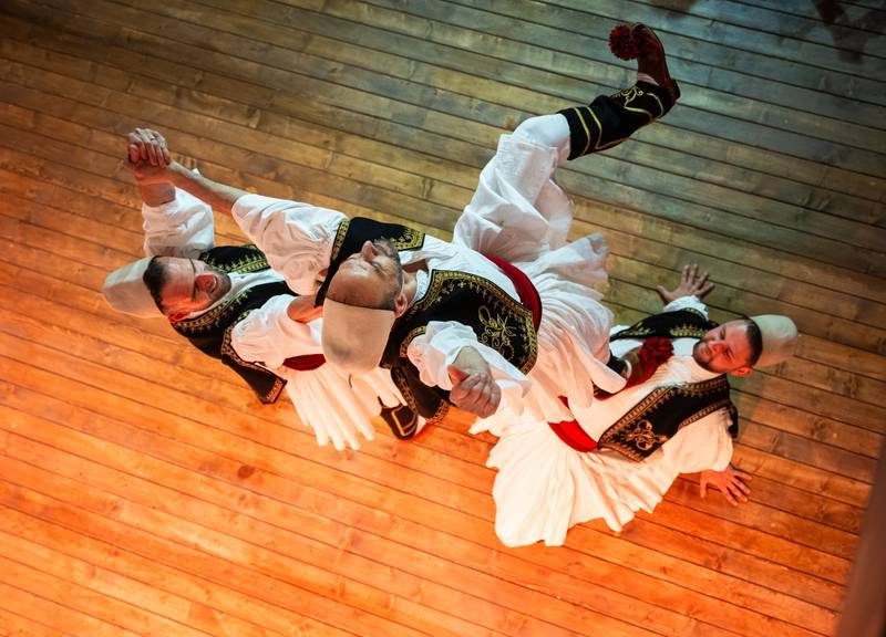 Danseurs albanais en costume traditionnel exécutant une danse folklorique sur une scène en bois