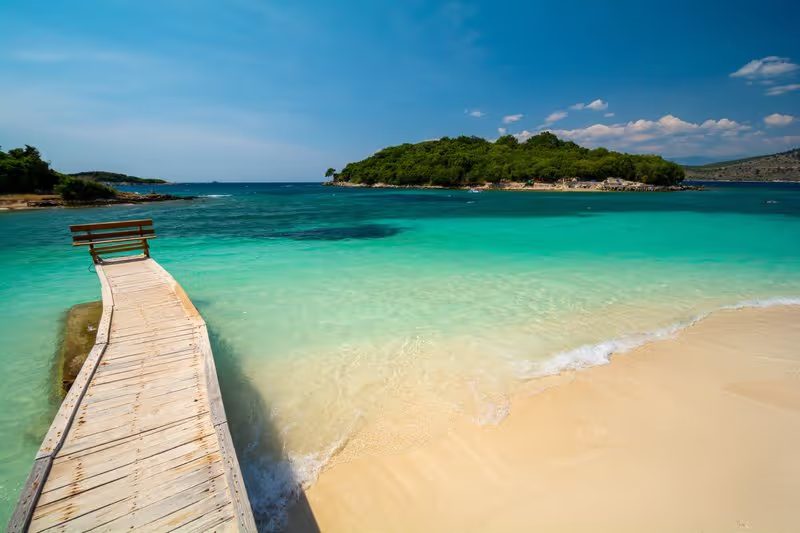 Ponton en bois menant à une plage de sable fin avec des eaux turquoise à Ksamil, Albanie. 