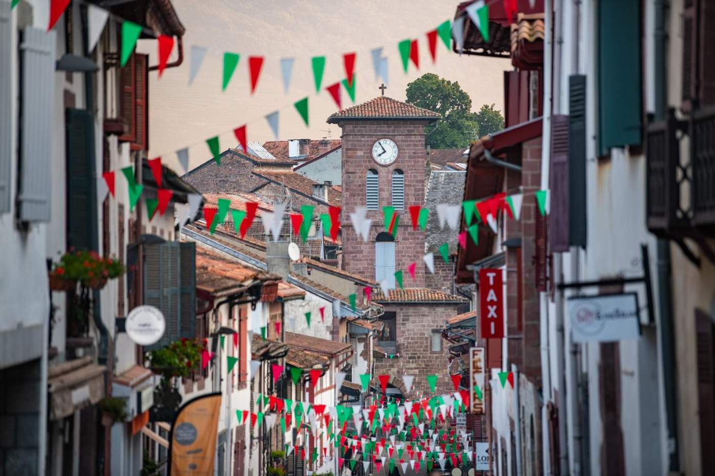 Rue principale de Saint-Jean-Pied-de-Port décorée de guirlandes tricolores rouge, blanc et vert pour les fêtes, avec le clocher de l'église en arrière-plan – Pays Basque