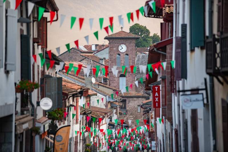 Rue principale de Saint-Jean-Pied-de-Port décorée de guirlandes tricolores rouge, blanc et vert pour les fêtes, avec le clocher de l'église en arrière-plan – Pays Basque