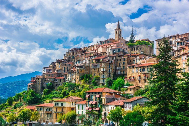 Vue pittoresque du village perché d’Apricale, avec ses maisons en pierre traditionnelles entourées de collines verdoyantes sous un ciel bleu