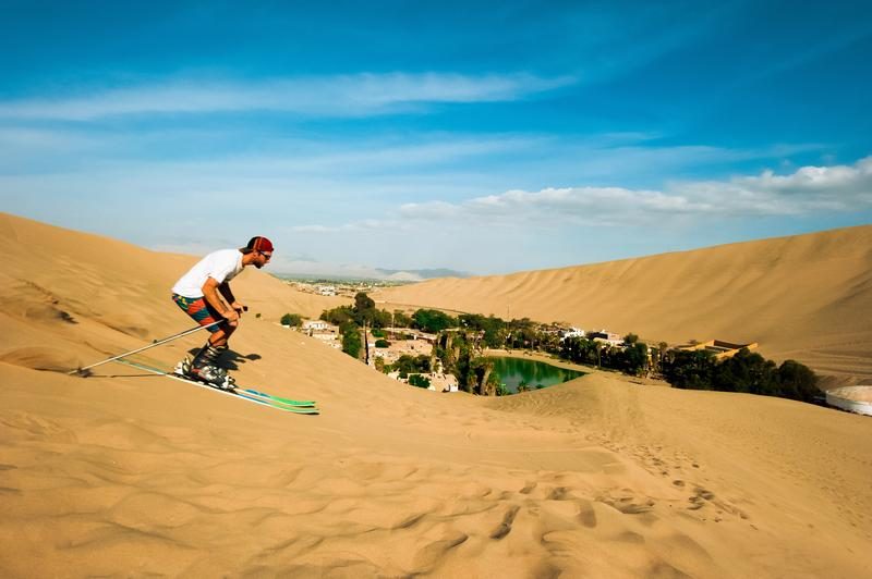 Voyageur pratiquant le sandboard sur les dunes de Huacachina avec vue sur l’oasis.