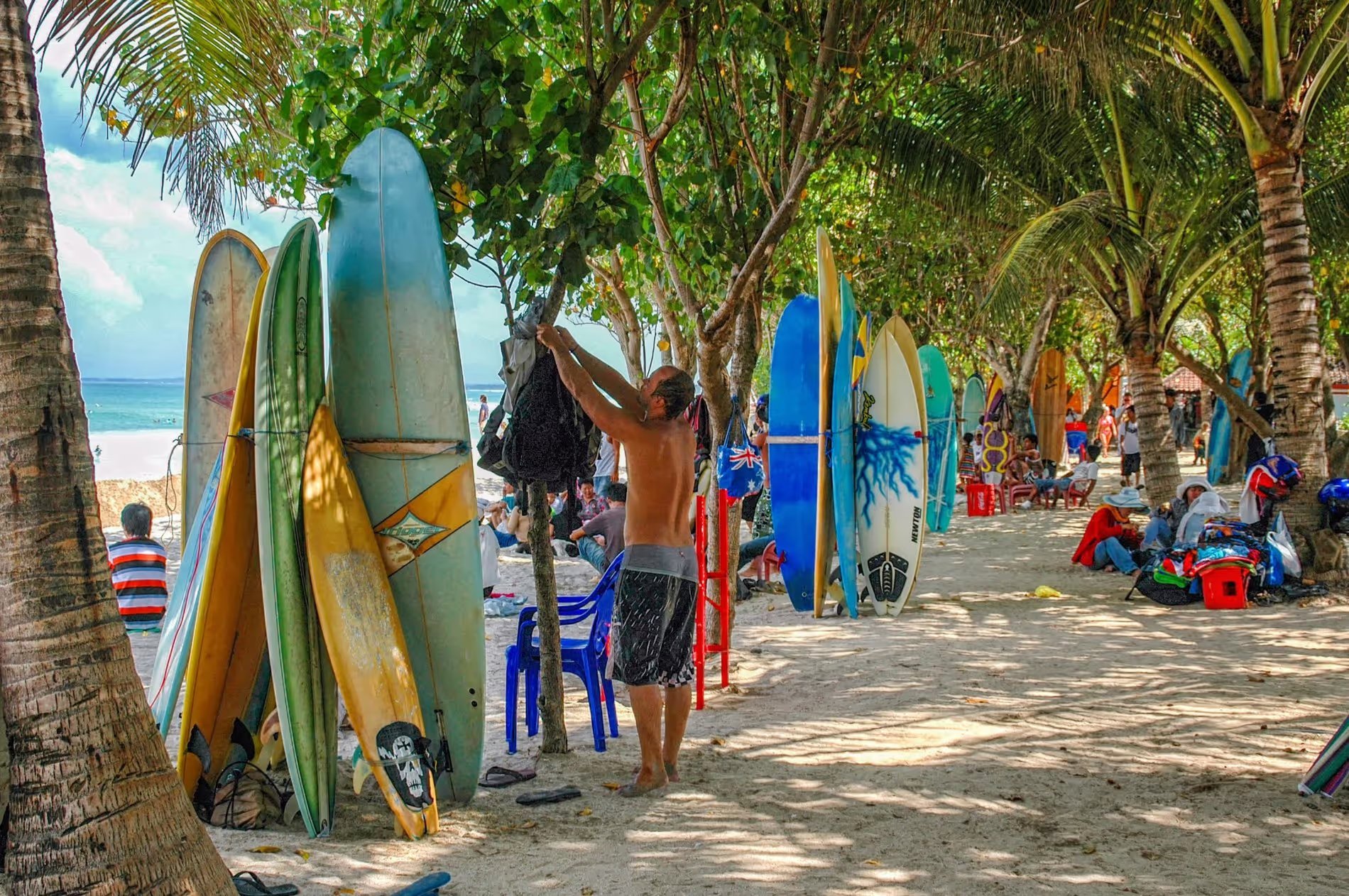 Des planches de surf alignées sur une plage de Canggu, entourées de palmiers et de surfeurs préparant leurs équipements.