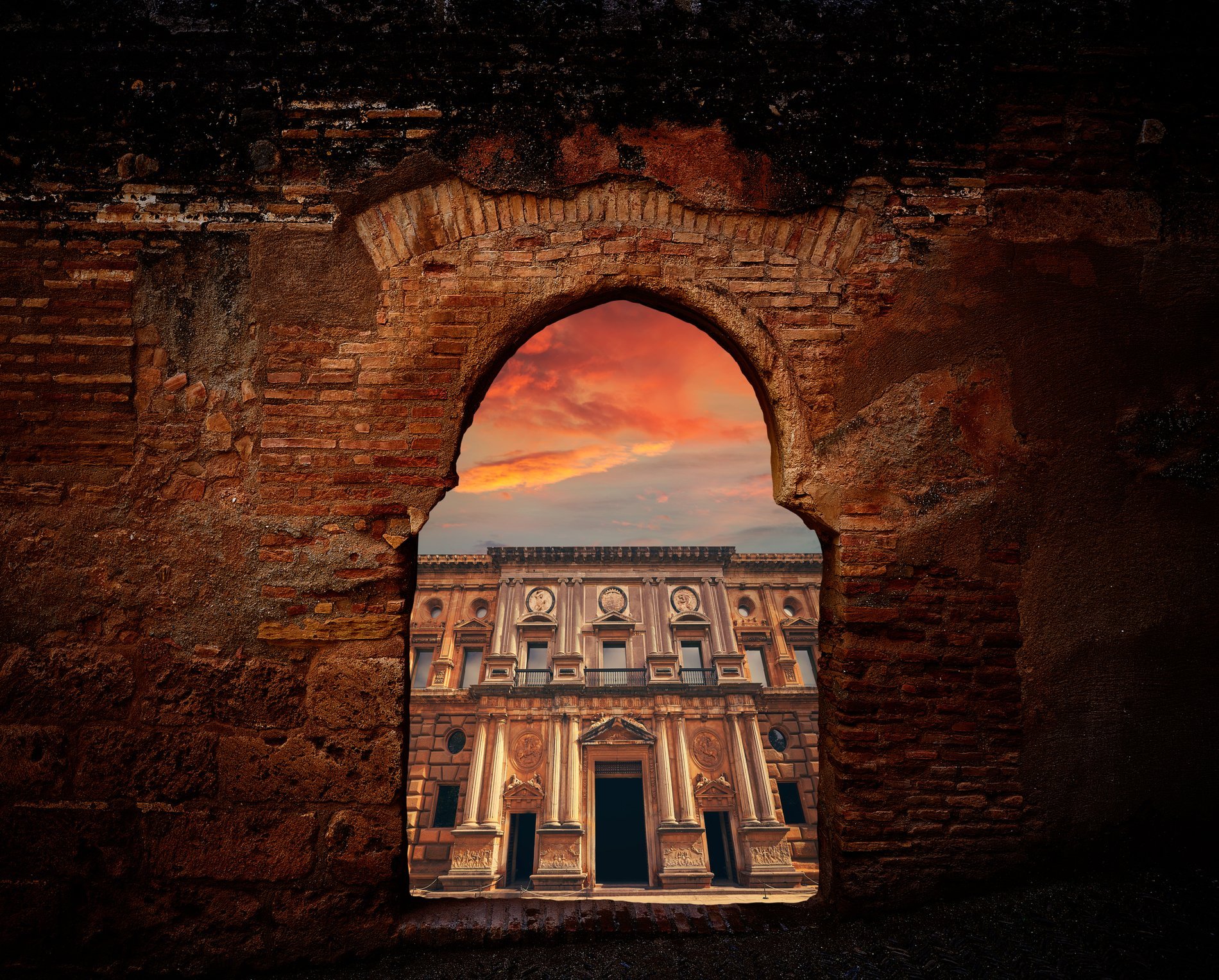 Vue encadrée par une arche en pierre sur un palais de la Renaissance dans l'Alhambra de Grenade, au coucher du soleil, avec un ciel coloré en arrière-plan.