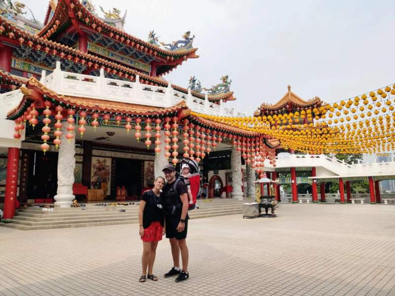 Maud, Cyril et Anna visitant un temple chinois magnifiquement décoré à Kuala Lumpur, en Malaisie, avec des lanternes colorées suspendues en arrière-plan.