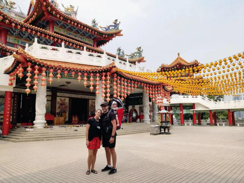 Maud, Cyril et Anna visitant un temple chinois magnifiquement décoré à Kuala Lumpur, en Malaisie, avec des lanternes colorées suspendues en arrière-plan.