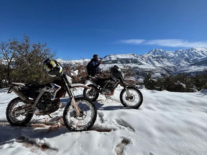 Deux motos enduro garées dans la neige face aux sommets de l’Atlas marocain