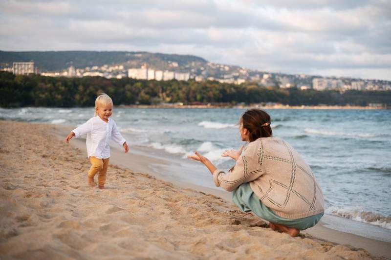 Mère accroupie tendant les bras vers son jeune enfant qui court sur une plage en bord de mer