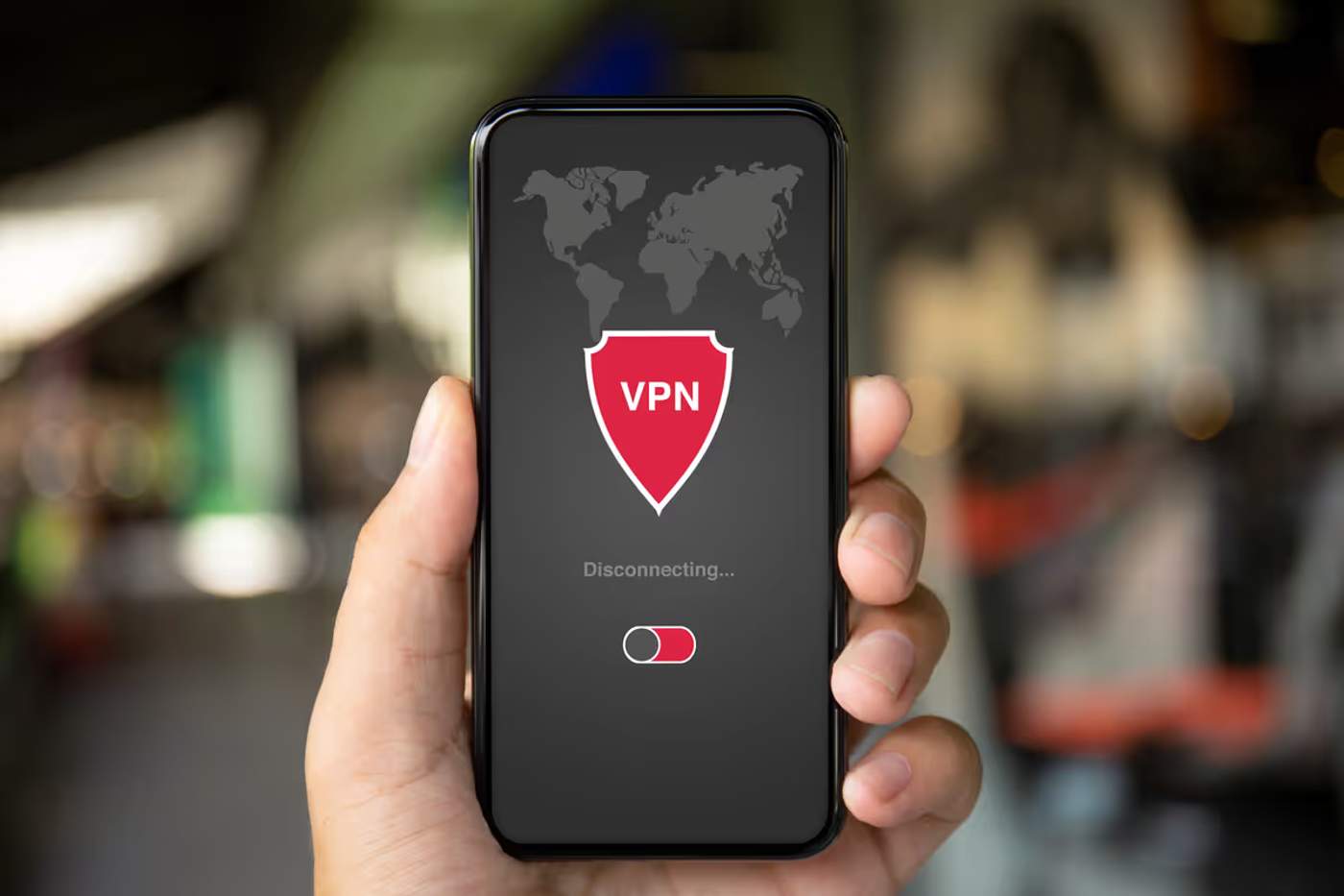 Main tenant un smartphone affichant une application VPN en cours de déconnexion avec un bouclier rouge et une carte du monde en arrière-plan