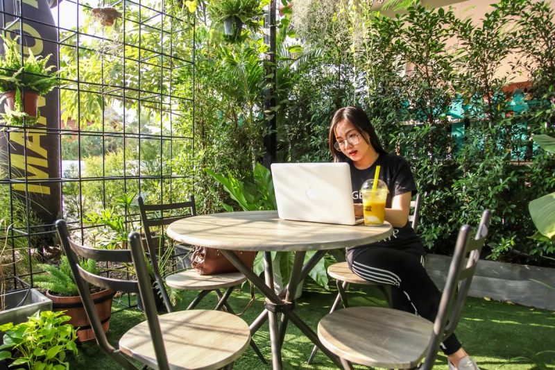 Une femme qui travaille sur un ordinateur portable dans un lieu rempli de plantes.