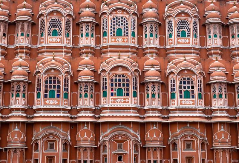Façade rose ornée du Palais des Vents à Jaipur, avec ses nombreuses fenêtres décorées typiques de l’architecture rajput.