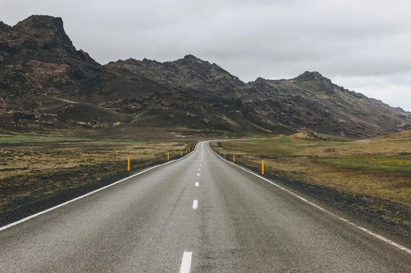 Route droite à travers un paysage volcanique sous un ciel nuageux, road trip en Islande