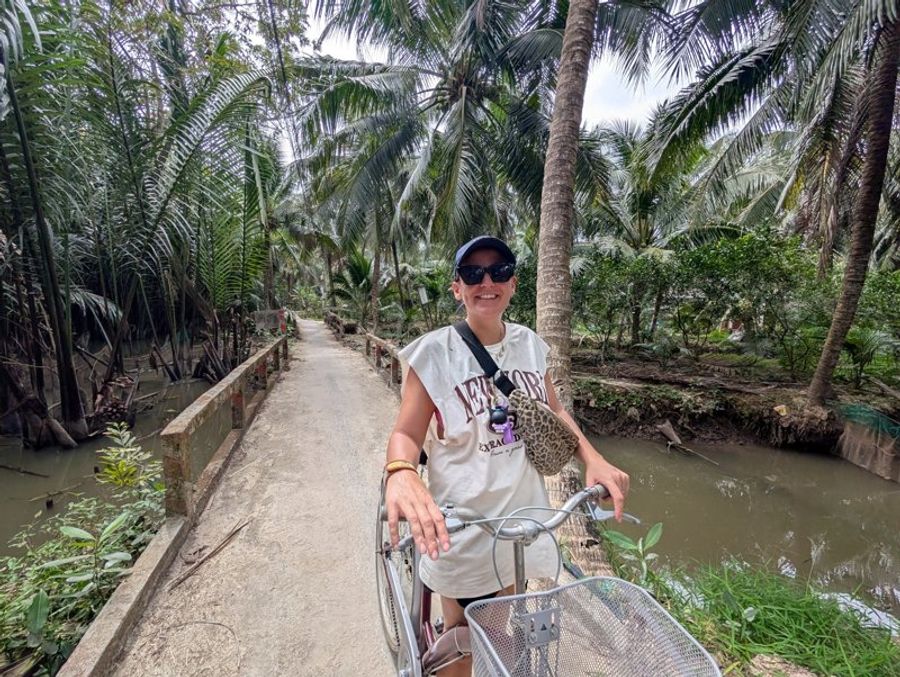 Voyageuse à vélo sur un petit chemin entre canaux et cocotiers dans la campagne de Ben Tre.
