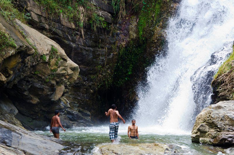 Chute d’eau se déversant sur des rochers avec des personnes en train de se baigner dans une piscine naturelle.