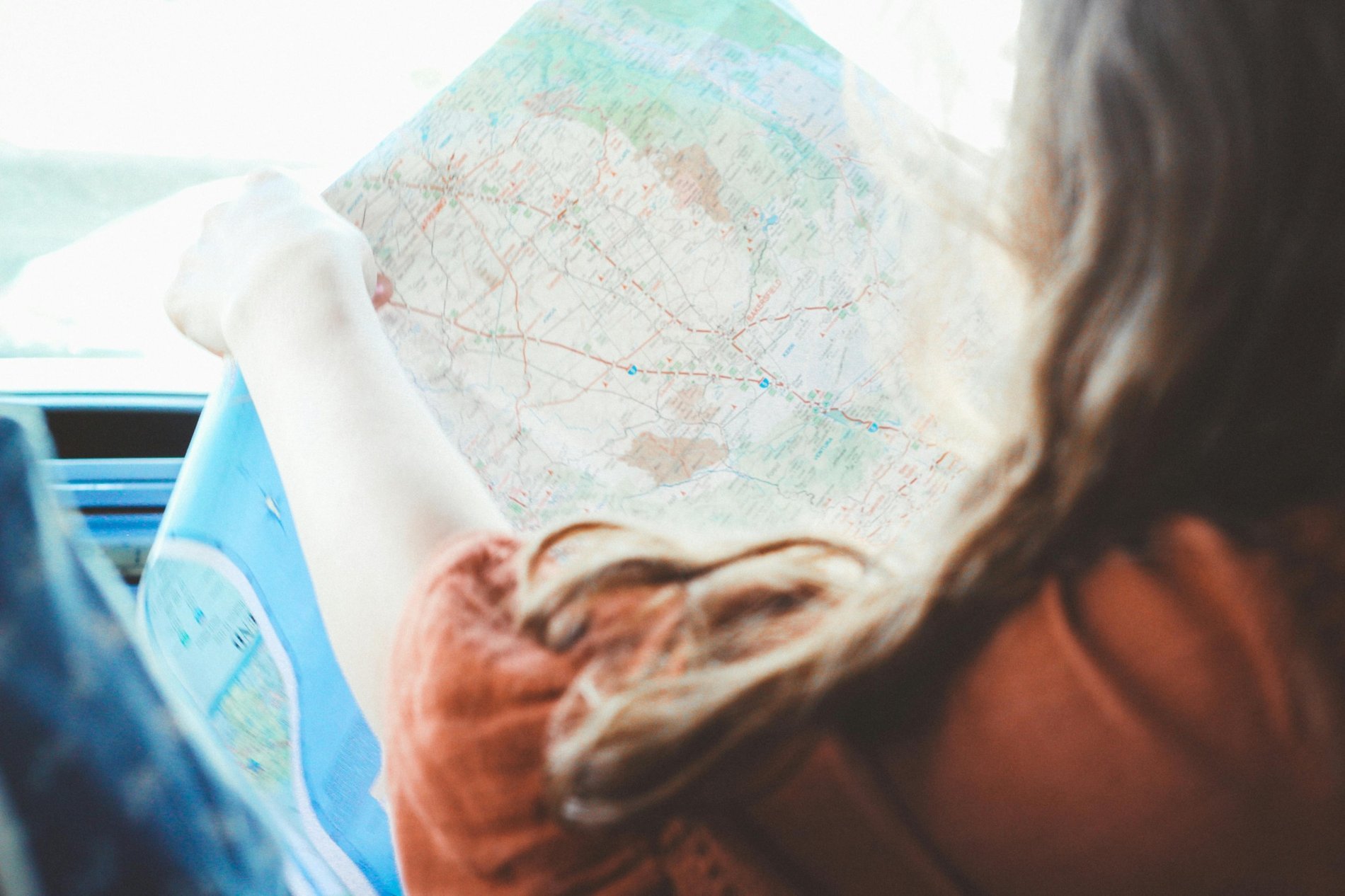 Personne en voyage tenant une carte routière, vue depuis l'intérieur d'une voiture.