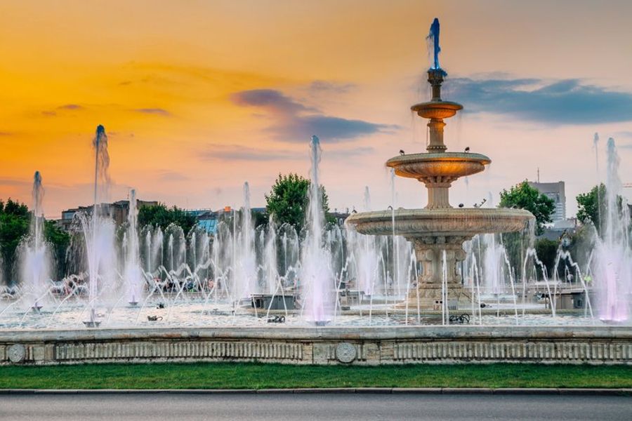 Spectacle de fontaines illuminées sur la place Unirii à Bucarest, jaillissant devant un ciel de coucher de soleil.