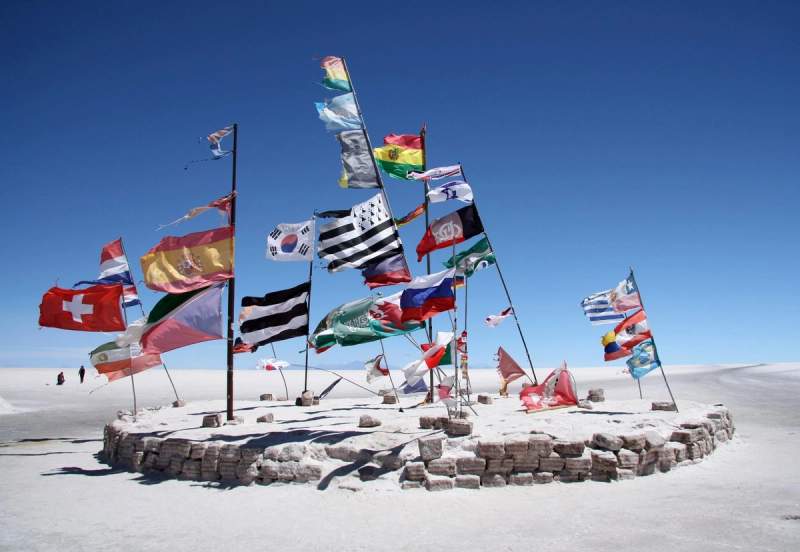 Plusieurs drapeaux internationaux flottant dans un désert salé sous un ciel bleu clair à Salar de Uyuni, Bolivie.