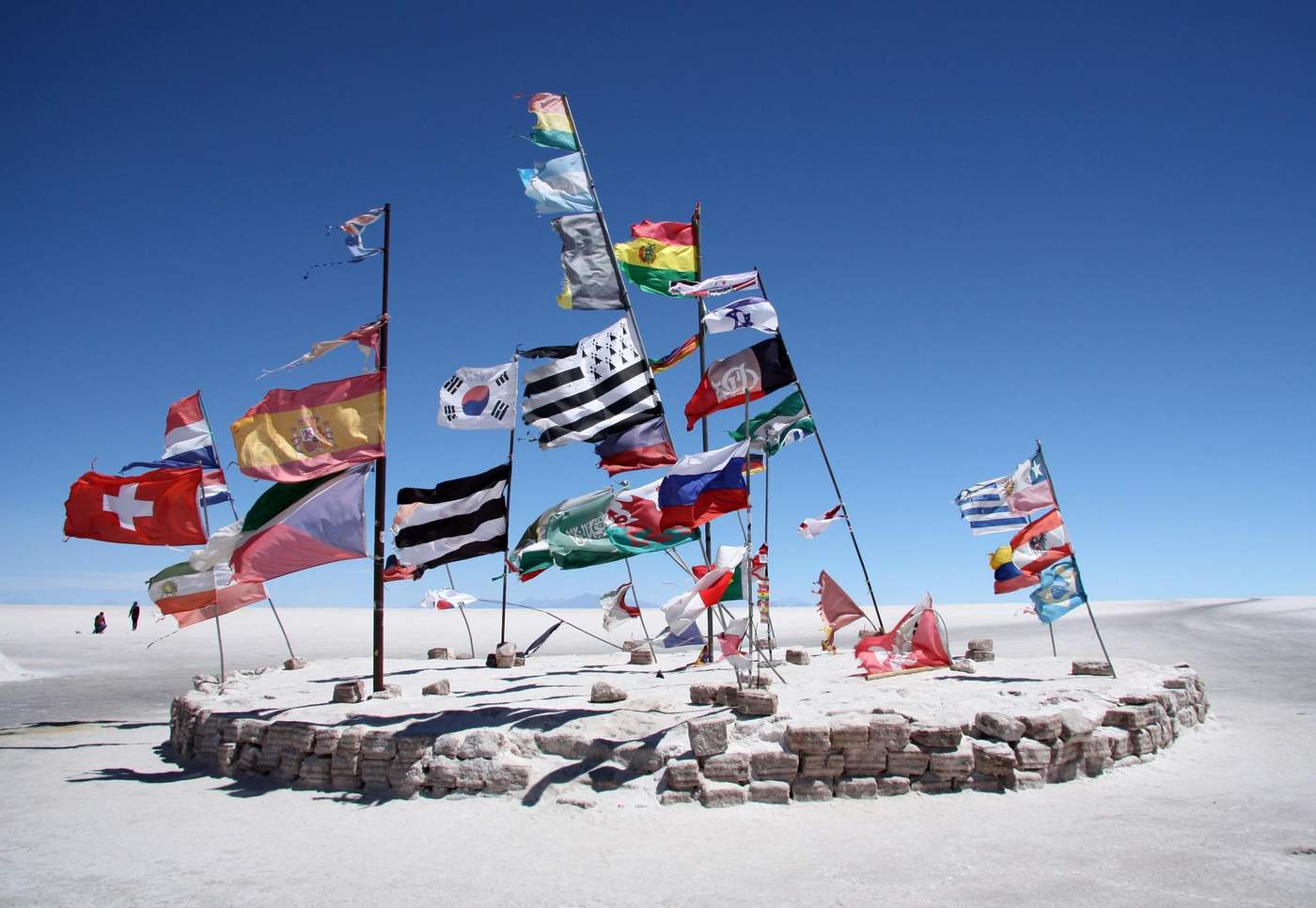 Plusieurs drapeaux internationaux flottant dans un désert salé sous un ciel bleu clair à Salar de Uyuni, Bolivie.