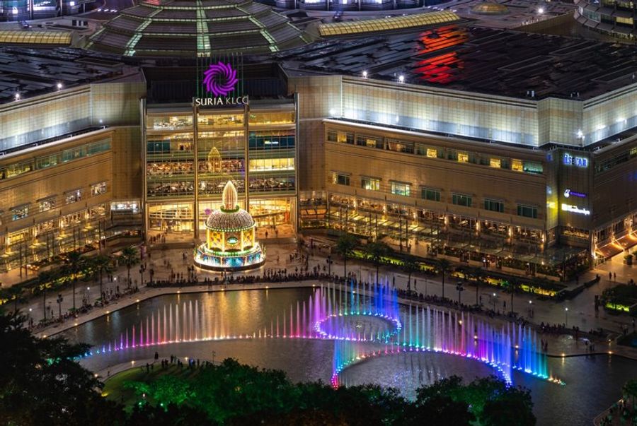 Centre commercial Suria KLCC avec une fontaine colorée et illuminée en soirée.