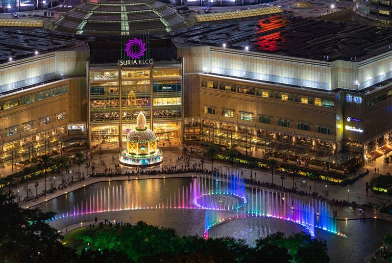 Centre commercial Suria KLCC avec une fontaine colorée et illuminée en soirée.