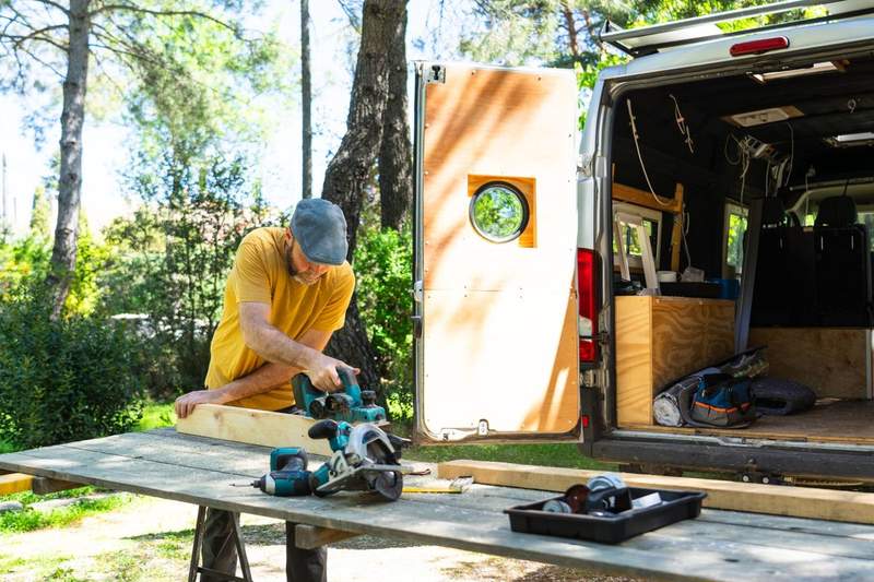 Artisan aménageant l’intérieur d’un van avec des panneaux en bois, en plein air, lors d’un projet de vanlife.
