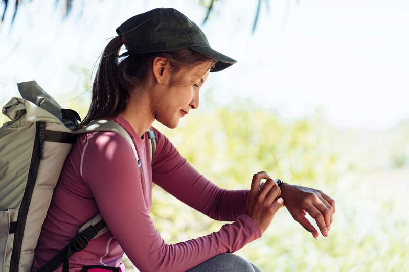 Jeune randonneuse consultant sa montre connectée en pleine nature pendant un voyage.