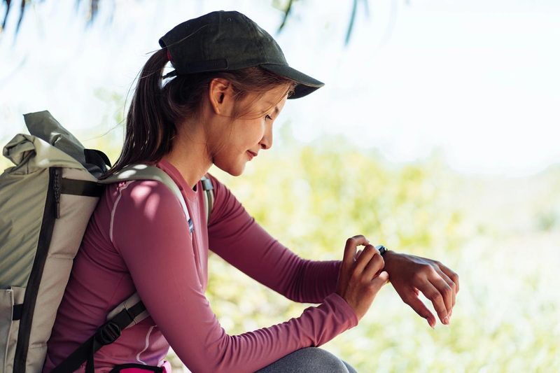 Jeune randonneuse consultant sa montre connectée en pleine nature pendant un voyage.