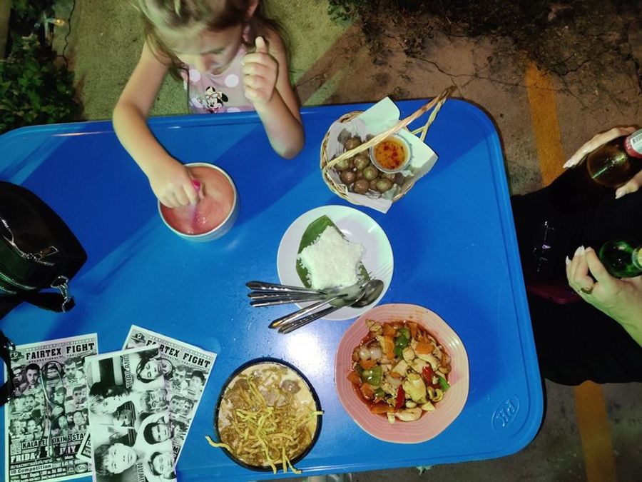 Anna mangeant à une table bleue avec divers plats thaïlandais de street food.