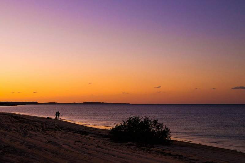 Deux personnes pêchent au bord de l’eau sur une plage isolée au coucher du soleil, sur la côte Ouest de l’Australie.