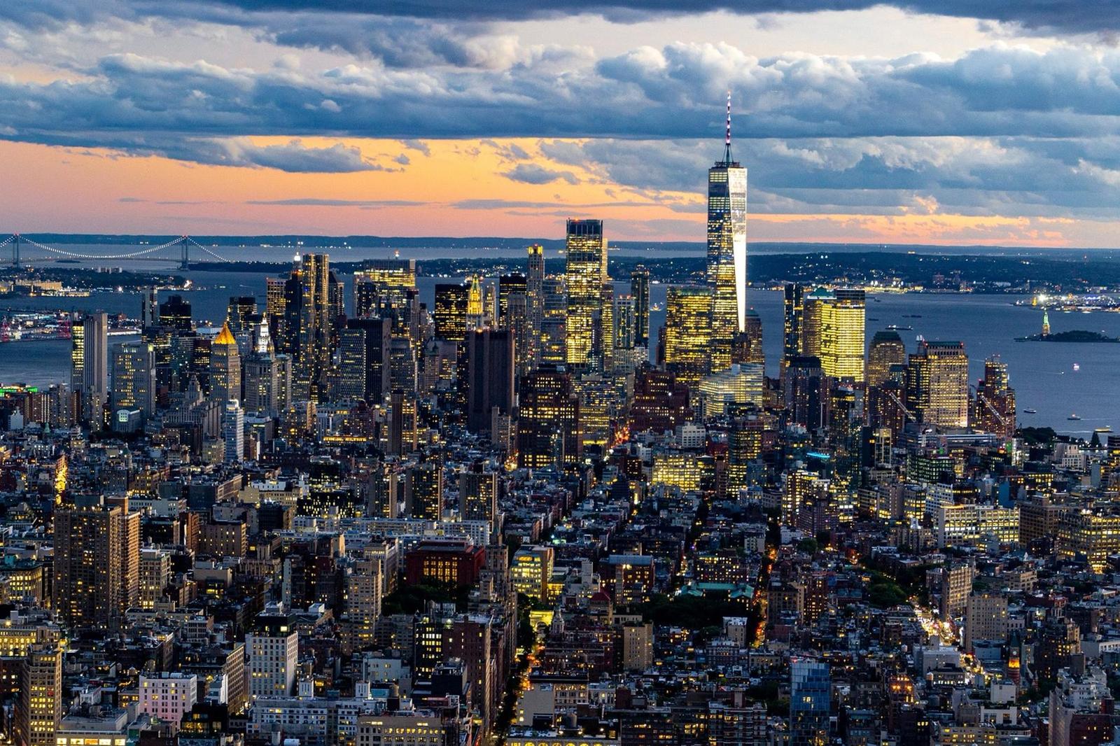 Vue panoramique de la ville de New York au crépuscule, avec des gratte-ciels illuminés et un ciel nuageux.