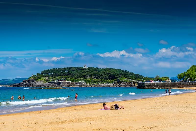 Plage de Santander avec des baigneurs et une vue sur une colline en arrière-plan.