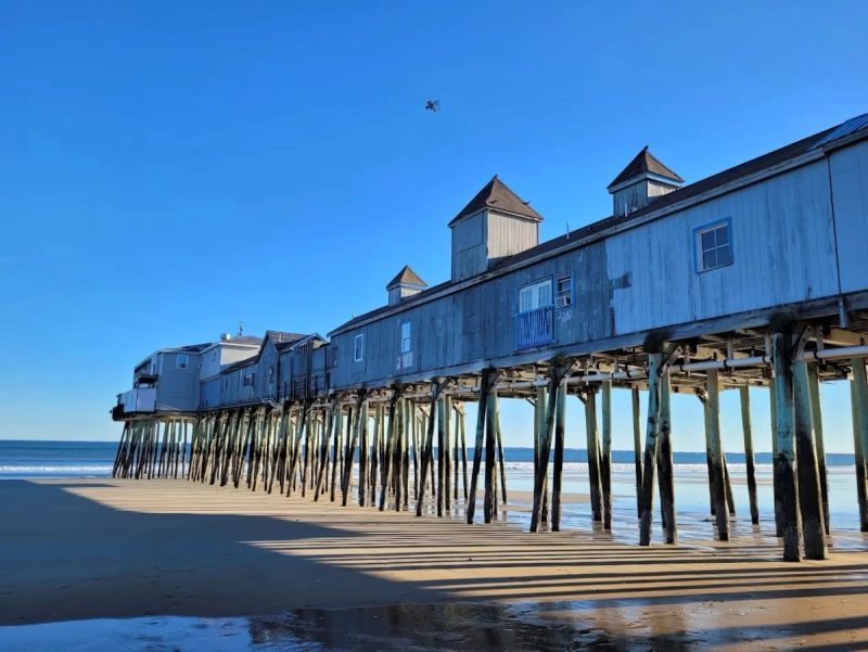 Vieux ponton en bois sur la plage à Old Orchard Beach, avec des bâtiments sur pilotis au-dessus de la mer, ciel bleu en arrière-plan