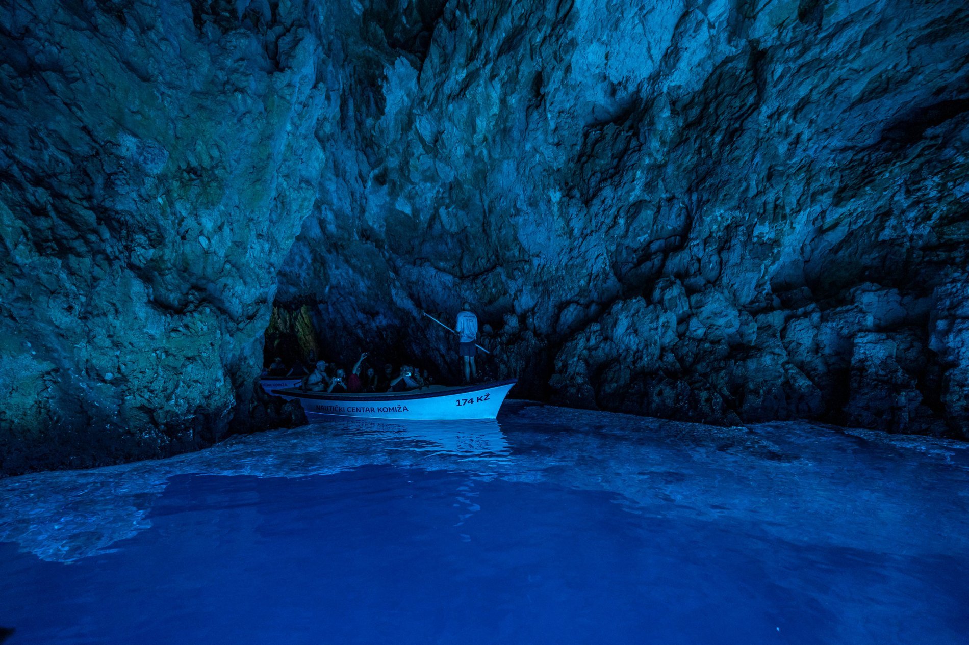Un petit bateau avec des touristes à l'intérieur de la grotte bleue de Biševo, baigné par une lumière bleue éclatante.