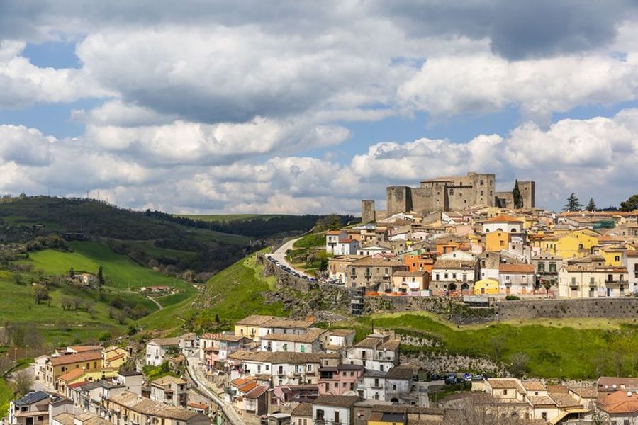 Vue panoramique de la ville de Melfi avec son château historique et ses maisons colorées sur une colline verdoyante.