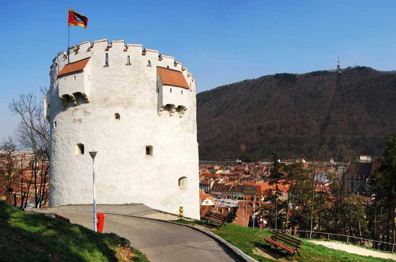 Tour de rempart blanche avec créneaux, surplombant la ville de Brașov et les collines environnantes.