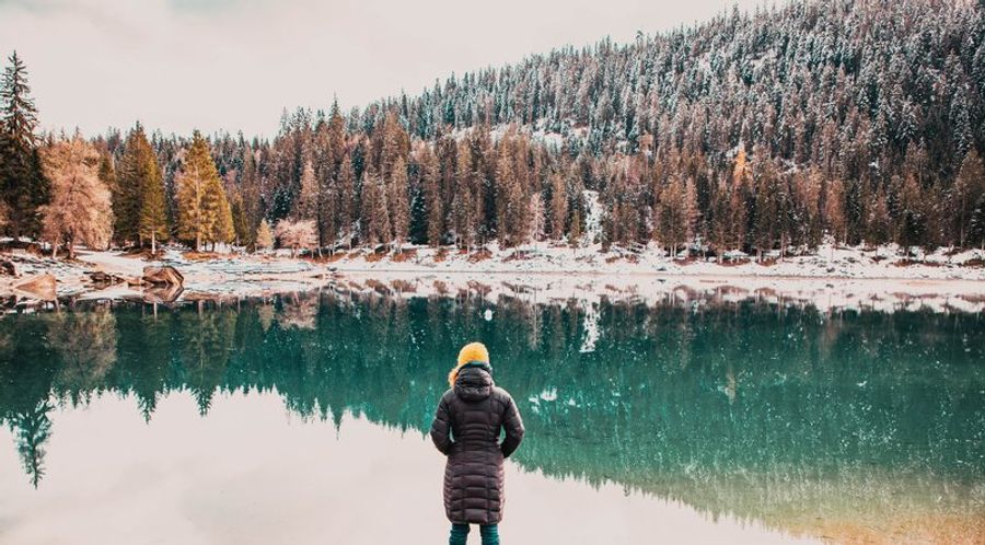Personne contemplant un lac de montagne en hiver, entouré de forêts enneigées, illustrant la quiétude du slow travel en nature.