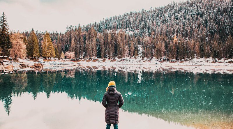 Personne contemplant un lac de montagne en hiver, entouré de forêts enneigées, illustrant la quiétude du slow travel en nature.