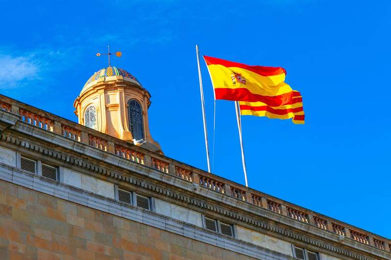 Drapeau de l’Espagne et drapeau catalan flottant sur un bâtiment historique à Barcelone.