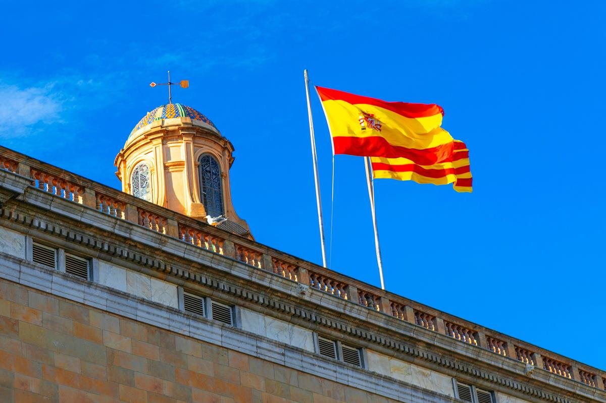 Drapeau de l’Espagne et drapeau catalan flottant sur un bâtiment historique à Barcelone.