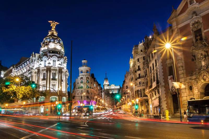 Avenue Gran Vía à Madrid illuminée la nuit, avec des bâtiments historiques et des lumières de circulation.
