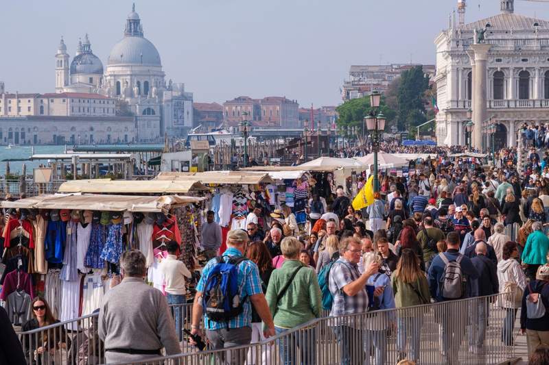 Foule de touristes sur une promenade à Venise, avec des stands de souvenirs et la basilique Santa Maria della Salute en arrière-plan