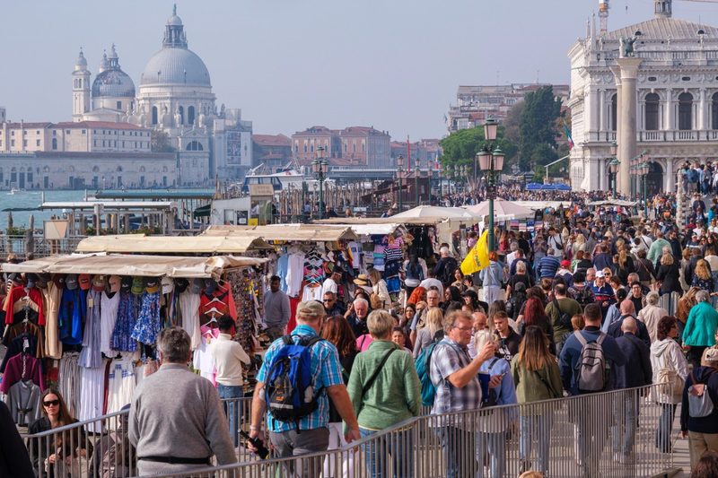 Foule de touristes sur une promenade à Venise, avec des stands de souvenirs et la basilique Santa Maria della Salute en arrière-plan