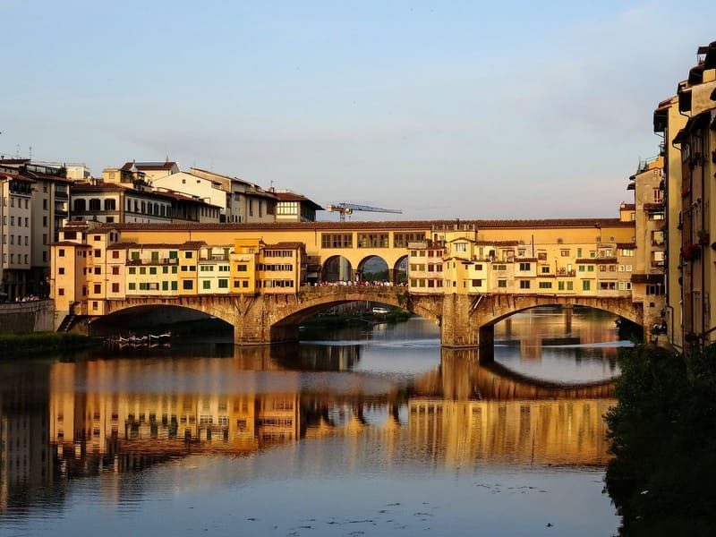Le célèbre Ponte Vecchio de Florence au coucher du soleil, reflétant ses arches et ses boutiques sur le fleuve Arno.