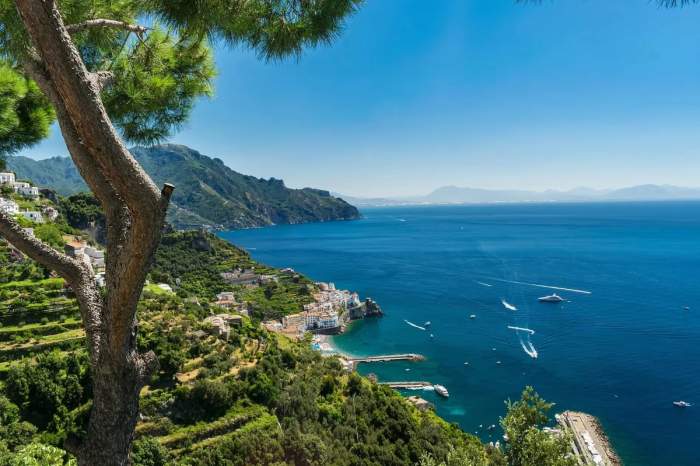 Vue panoramique de la côte amalfitaine en Italie, avec des montagnes verdoyantes et une mer bleue scintillante sous un ciel dégagé.