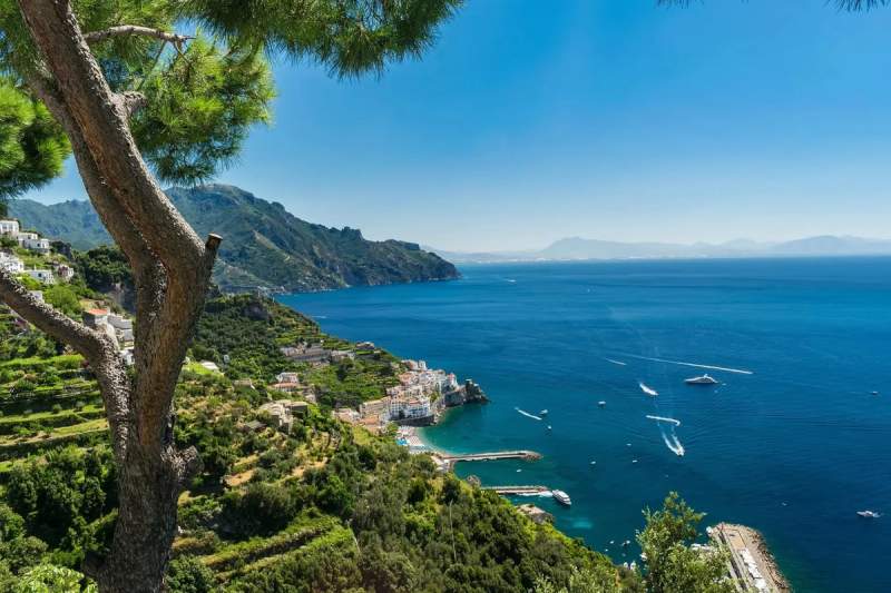 Vue panoramique de la côte amalfitaine en Italie, avec des montagnes verdoyantes et une mer bleue scintillante sous un ciel dégagé.