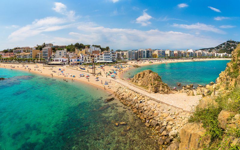 Vue panoramique de la plage de Blanes avec des parasols et des immeubles en arrière-plan.