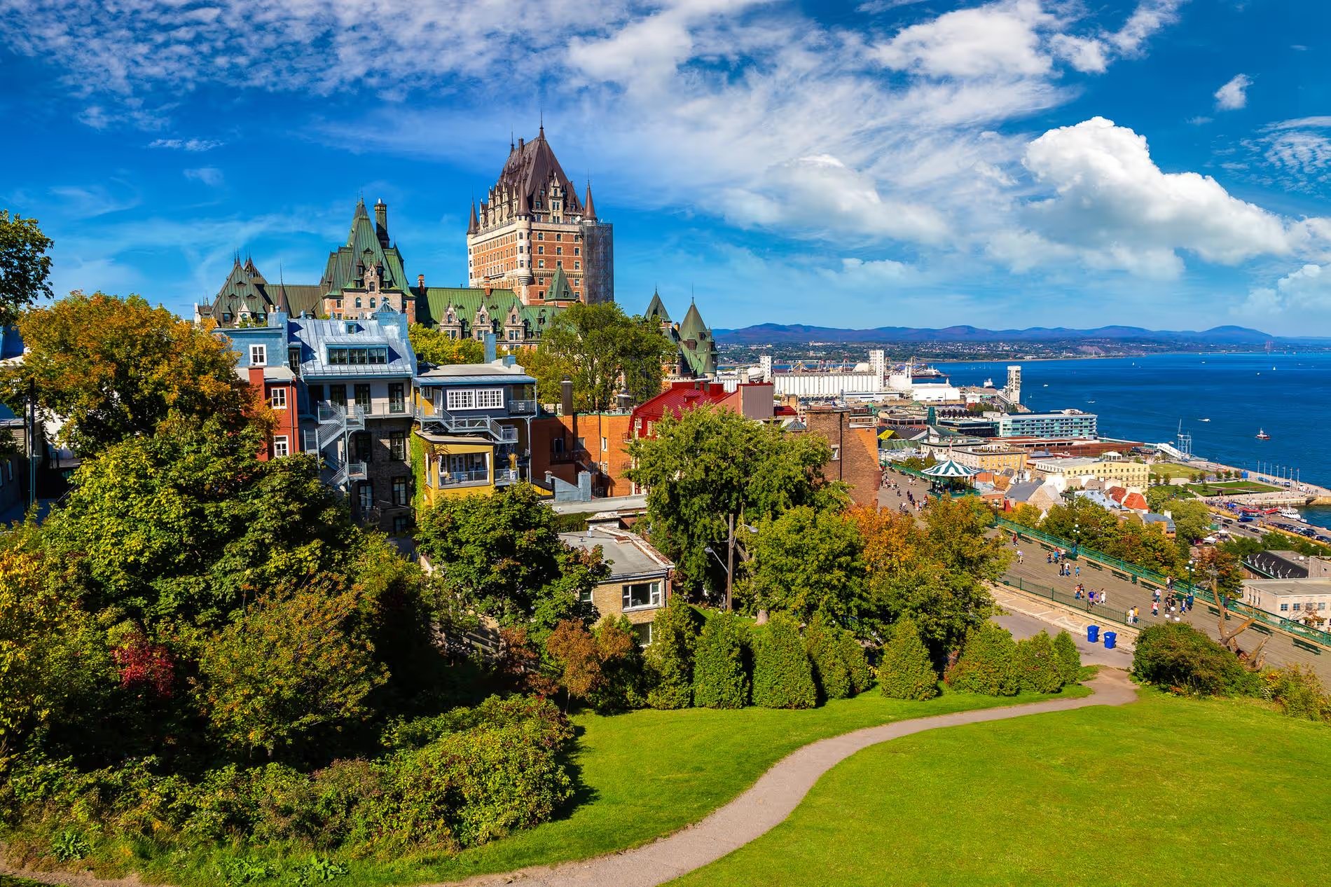 Vue panoramique sur la ville de Québec avec le célèbre château Frontenac et le fleuve Saint-Laurent, entouré de verdure et d'architecture historique.