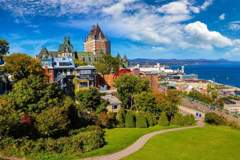 Vue panoramique sur la ville de Québec avec le célèbre château Frontenac et le fleuve Saint-Laurent, entouré de verdure et d'architecture historique.